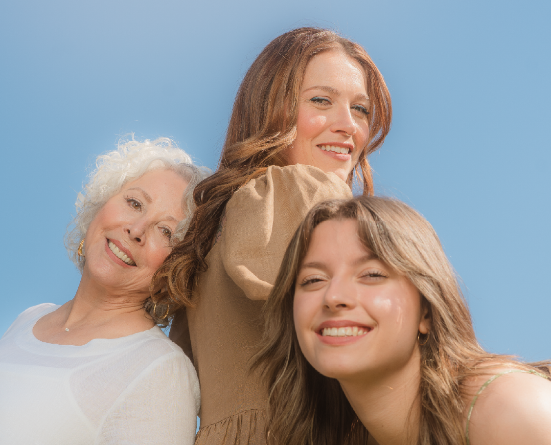 Group of three generations of women smiling with sky blue background.