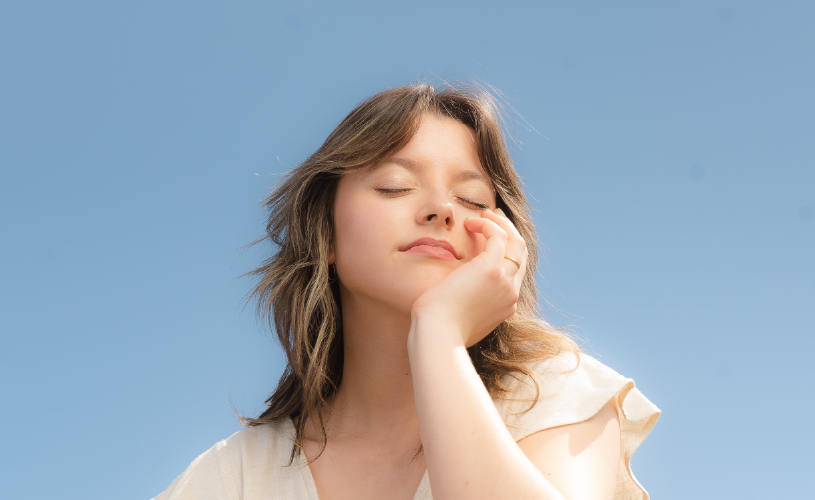 Young woman closeup. She's touching her face with a blue sky background.
