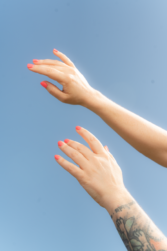 Nevaeh Day Spa hands in sky with bright orange painted nails.