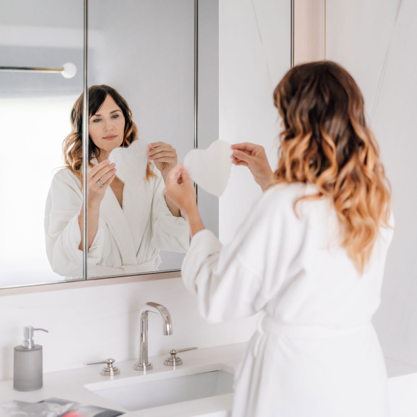 SOKE Chest treatment: image shows a woman wearing a white robe looking the in mirror about to apply the mask.