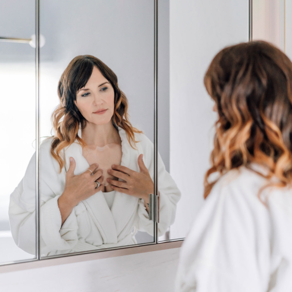 SOKE Chest treatment: image shows a woman wearing a white robe looking the in mirror applying the mask.